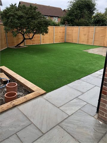 Green lawn surrounded by garden paving and timber fencing