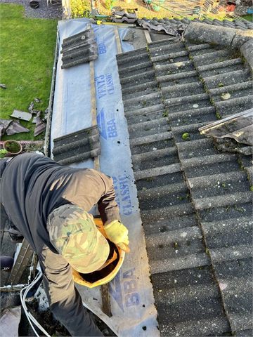 A worker attending to a roof surface beside guttering