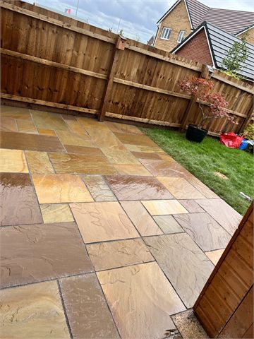 Multicoloured garden paving beside lawn and timber fencing