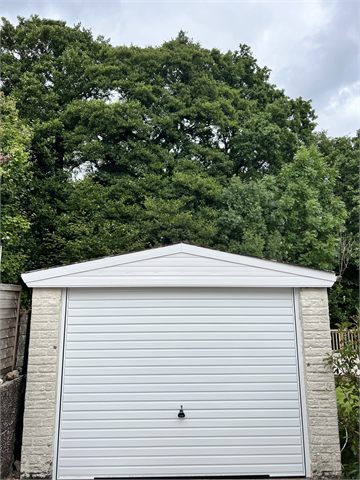 Garage roof and white garage door beneath garden trees